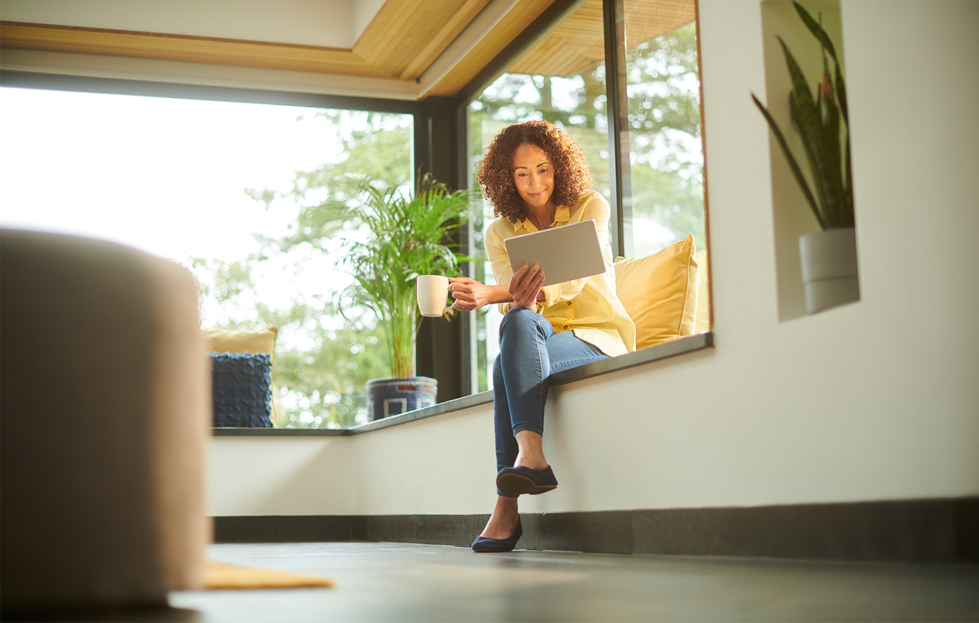 Entspannter Moment auf der Fensterbank Frau auf einer Fensterbank mit großen Fenstern, entspannt mit einer Tasse Kaffee.
